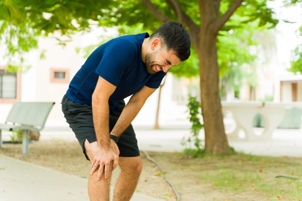 Man holding his knee in pain while walking outdoors, showing symptoms of arthritis or wear-and-tear joint damage; used for educational blog by Dr. Ashish Suryawanshi, Orthopaedic Surgeon in Pune.