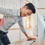 Person sitting at a desk with poor posture causing back pain